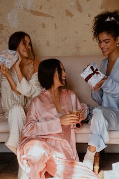 three women in robes sitting on a couch and one is holding a gift while the other holds a present