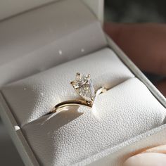 a diamond ring in a white box with someone's hand holding it up to the camera