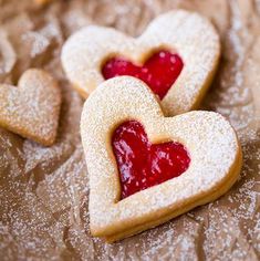 some heart shaped cookies are on a table with powdered sugar and jelly in the shape of hearts