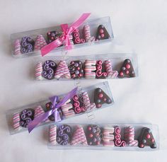 three boxes filled with chocolate covered pretzels on top of a white table next to a pink ribbon