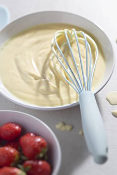 a bowl filled with cream and strawberries next to a whisk on a table