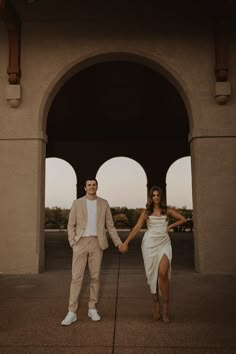 a man and woman holding hands in front of arches