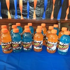 several bottles of nerf are lined up on a blue tablecloth with orange streamers