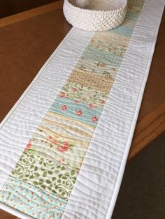 the table runner is decorated with colorful quilts on it's sides and a white bowl sitting on top