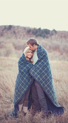 a man and woman wrapped in a blanket sitting on top of a grass covered field