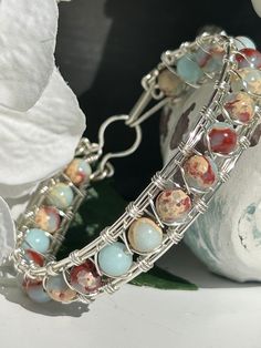 This boho bangle bracelet is inspired by the pure and natural beauty of the beach.  In fact, many of the products in my shop are handmade on the beach while savoring the cool breeze and calming ocean sounds. The gemstone, polished blue ocean jasper, boasts light blue, clay red, tan and cream hues and is absolutely beautiful  In keeping with its symbolism, ocean jasper is said to provide calm, uplifting energy to the holder in trying times, feeding into a more optimistic outlook on life.  The sto Boho Bangle Bracelets, Gemstone Bangle Bracelets, Diy Bangle Bracelets, Metal Art Jewelry, Wire Jewelry Patterns, Boho Bangle, Gemstone Bangle, Crystal Bangle, Diy Wire Jewelry