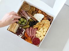 a box filled with lots of different types of cheeses and crackers next to a person's hand