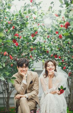 a man and woman sitting next to each other in front of trees with red flowers