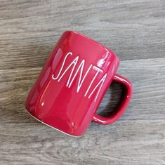 a red coffee mug with the word santa written on it sitting on a wooden surface