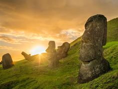 the sun is setting behind some moai statues on a grassy hill with rocks in the foreground