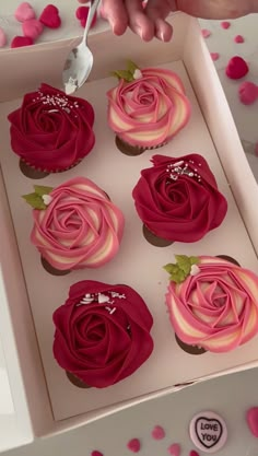 the cupcakes in the box are decorated with pink icing and rose petals