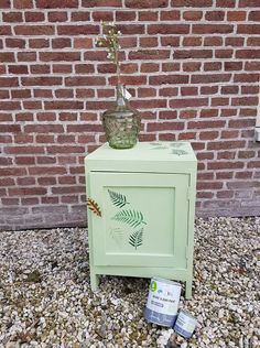 a green cabinet sitting on top of a gravel ground next to a red brick wall