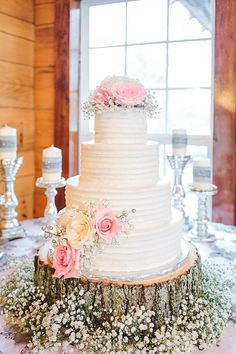 a white wedding cake with pink flowers and greenery on the top is surrounded by candles