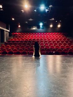 a person sitting on the floor in front of an empty auditorium filled with red chairs