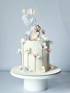 there is a cake with flowers and a teddy bear on top that has balloons in the air