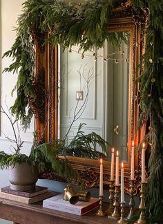 a mantle with candles and greenery on it in front of a mirror that is hanging from the ceiling