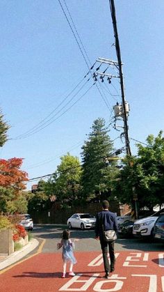 a father and daughter crossing the street in front of their car on a sunny day