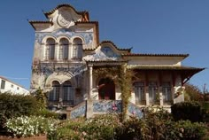 an old building with blue and white tiles on it's side, surrounded by greenery