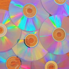 several cd's sitting on top of a wooden table next to each other with different colored discs around them