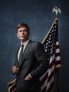 a man in a suit and tie standing next to an american flag