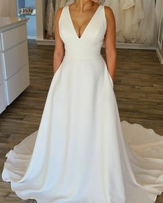 a woman standing in front of a mirror wearing a white wedding dress with deep v - neck