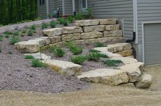 a large rock wall next to a house with flowers growing on the side and steps leading up to it