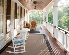 a porch with rocking chairs and table on the front porch, along with an area rug that looks like it could be covered in sun