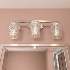 a bathroom mirror with two lights above it and a light fixture on the wall next to it