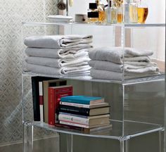 stack of folded white towels on clear shelf next to books and liquor bottles in bathroom