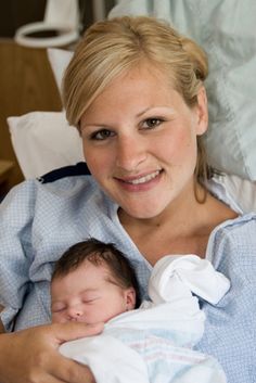 a woman holding a baby in her arms and smiling at the camera while sitting on a hospital bed