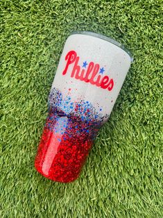 a red, white and blue cup with the word phillies painted on it sitting in grass