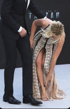 a man in a tuxedo helping a woman with her dress at the premiere