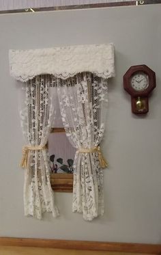 there is a clock on the wall next to a window with white lace curtains and drapes