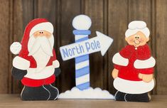 two santa claus figurines are standing next to a sign that says north pole