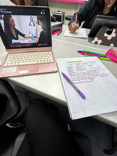 two women sitting at a table with laptops and notebooks in front of them