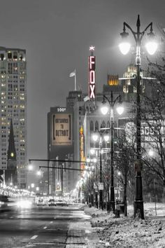 an empty city street at night with snow on the ground and tall buildings in the background