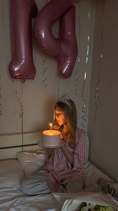 a woman sitting on her bed holding a cake with candles in front of her face