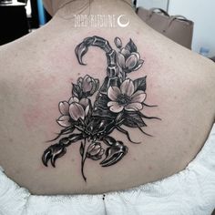 the back of a woman's neck with flowers and a snake tattoo on it