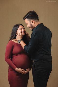 a pregnant woman standing next to a man in a black shirt and red dress with his hand on her belly