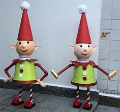 two elf statues standing next to each other in front of a white wall and brick floor