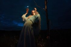 a woman reaching up to a tree at night