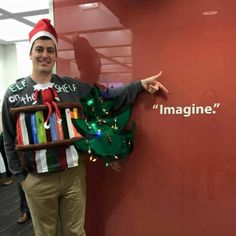 a man wearing a santa hat and holding a christmas tree in front of a red wall