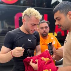 two men standing next to each other looking at a t - shirt on a cell phone