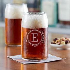 two glasses of beer sitting on top of a table next to nuts and a spoon