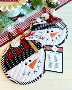 two snowmen are on the table with red and white checkered fabric, one has a tag that says merry christmas