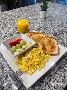 a white plate topped with eggs, toast and fruit next to a glass of orange juice