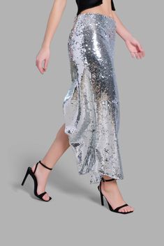 This mid-rise Silver Sequin Diagonal Maxi Skirt has an asymmetrical cut at the bottom. This skirt is noted for its uniqueness in design and its versatility. This product is styled with the Black Satin Arc-Cut Top. Spring Formal Asymmetrical Bottoms, Asymmetrical Bottoms For Formal Spring Occasions, Asymmetrical Bottoms For Spring Formal Events, Asymmetrical Bottoms For Spring Formal Occasions, Spring Party Midi Draped Skirt, Asymmetrical Skirt For Spring Party, Party Long Skirt With Side Slits, Party Skirt With Side Slits And Long Shape, Party Skirt With Side Slits And Long Length