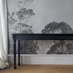 a black console table sitting in front of a wall with trees painted on the walls