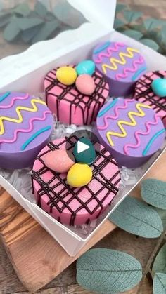 four decorated cupcakes sitting in a box on a wooden table next to leaves