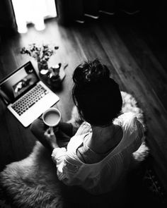 a woman sitting on the floor with a laptop and coffee cup in front of her